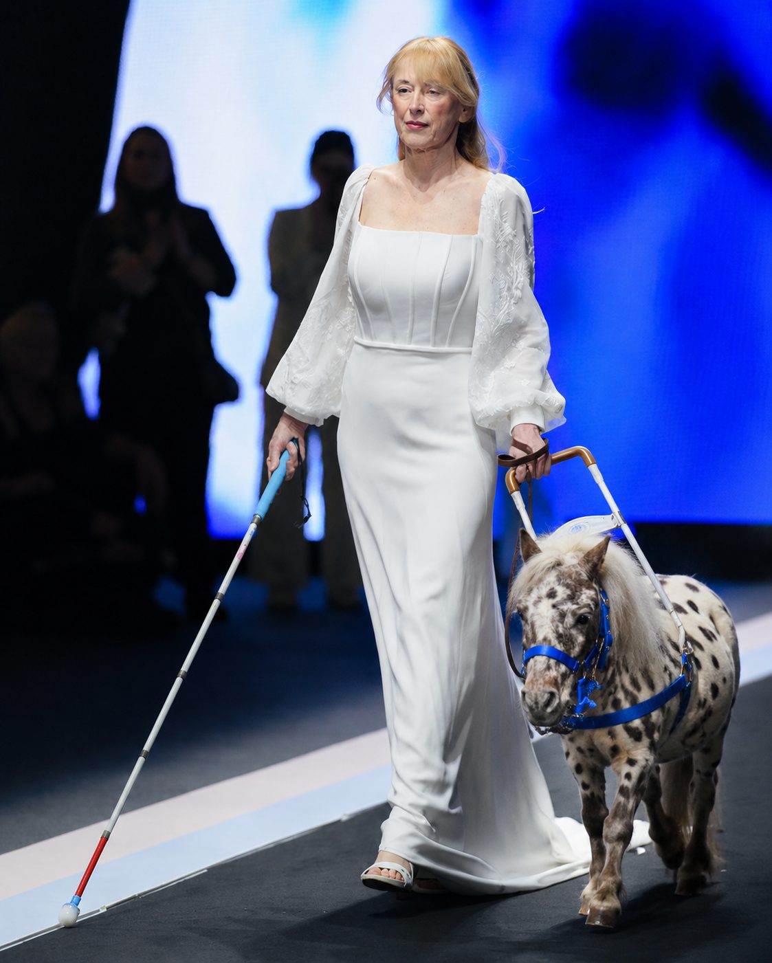 Modella in abito bianco guidata da un mini pony maculato con pettorina