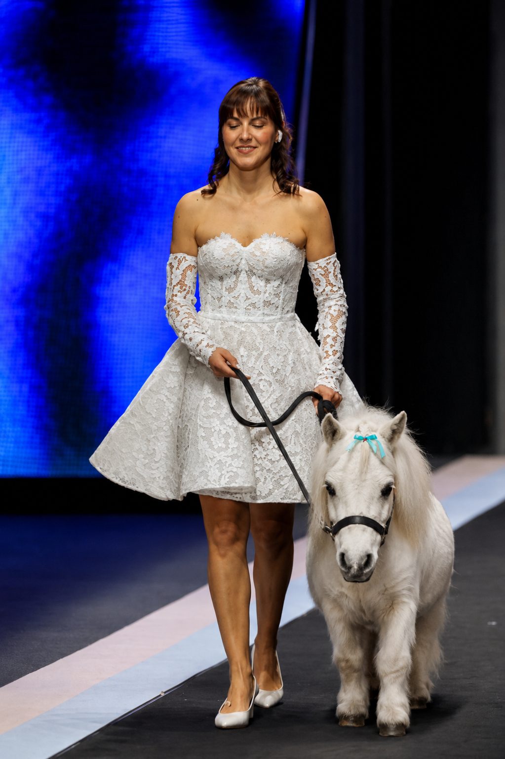 Florinda sfila in abito corto di pizzo con un mini pony bianco